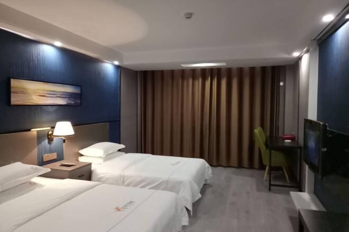 Een hotelkamer met twee bedden, een bureau, een stoel, een televisie en een schilderij aan de muur.