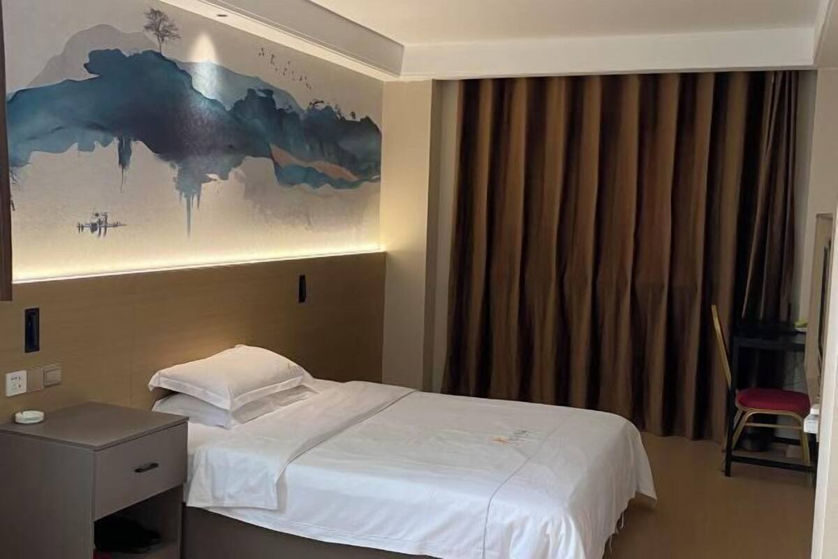 Een hotelkamer met een bed, een bureau, een stoel, een groot schilderij aan de muur en een raam met gordijnen.