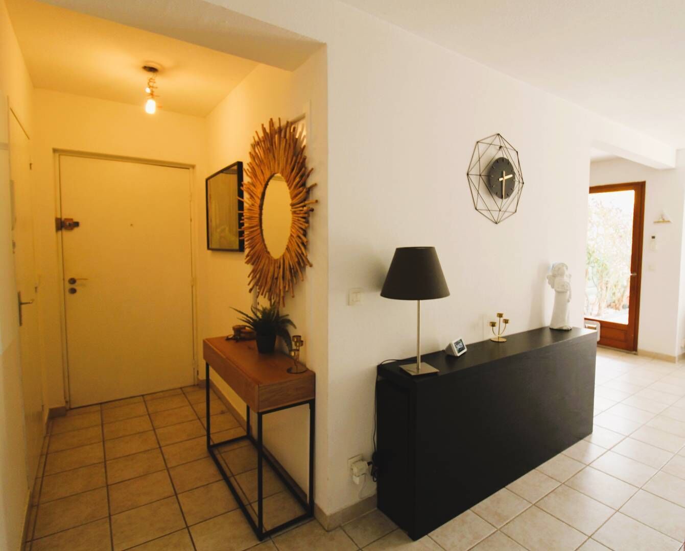 Um corredor com um banco de madeira, uma mesa preta, um relógio de parede e uma porta.