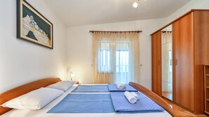 Une chambre double avec deux lits, une armoire en bois, un tableau au mur et une fenêtre avec des rideaux légers.