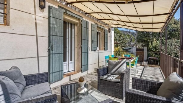 Ein möblierter Patio-Bereich mit Korbmöbeln, einem Glastisch und einer überdachten Sitzecke mit Blick auf die umliegende Landschaft.