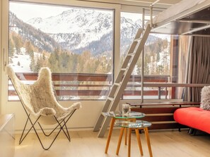 A room with a large window offering a mountain view, a chair, a glass table, and a red sofa.