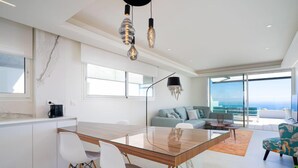 Un espace de vie moderne avec une table à manger en verre, des chaises blanches, un canapé et une vue sur l’océan.