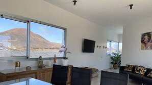 Una sala de estar moderna con un ventanal grande, un televisor de pantalla plana y un sofá negro con cojines estampados.