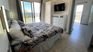 Un dormitorio con cama, televisión, armario y balcón.