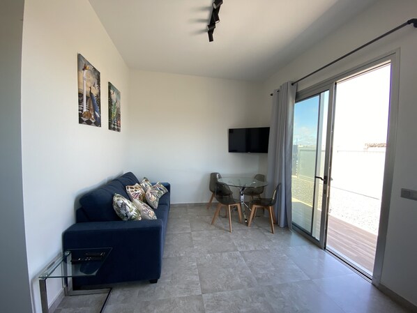 A modern living room with a sofa, a glass table, and chairs. A flat-screen TV is mounted on the wall. - Villa at the Foot of the Volcano (Lajares)