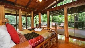 A wooden room with a bed, a ceiling fan, and large windows.