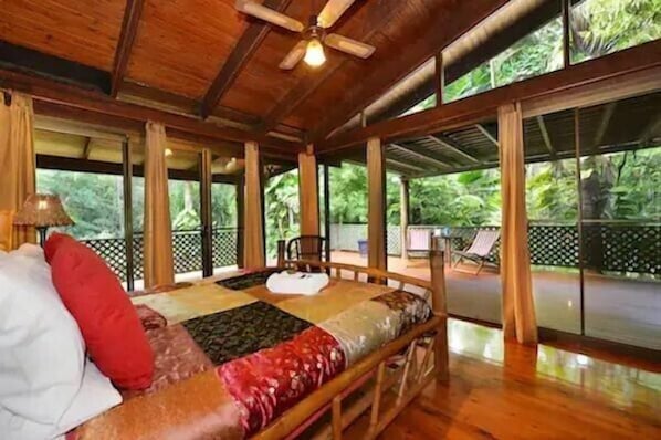 A wooden room with a bed, a ceiling fan, and large windows.