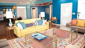 Una sala de estar con un sofá amarillo, una mesa de centro de vidrio y una alfombra colorida.
