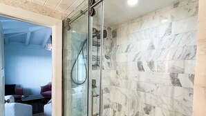 Une salle de bain moderne dotée d’une douche à parois de verre, de carreaux de marbre et d’un espace détente visible, comprenant un canapé et une table basse.