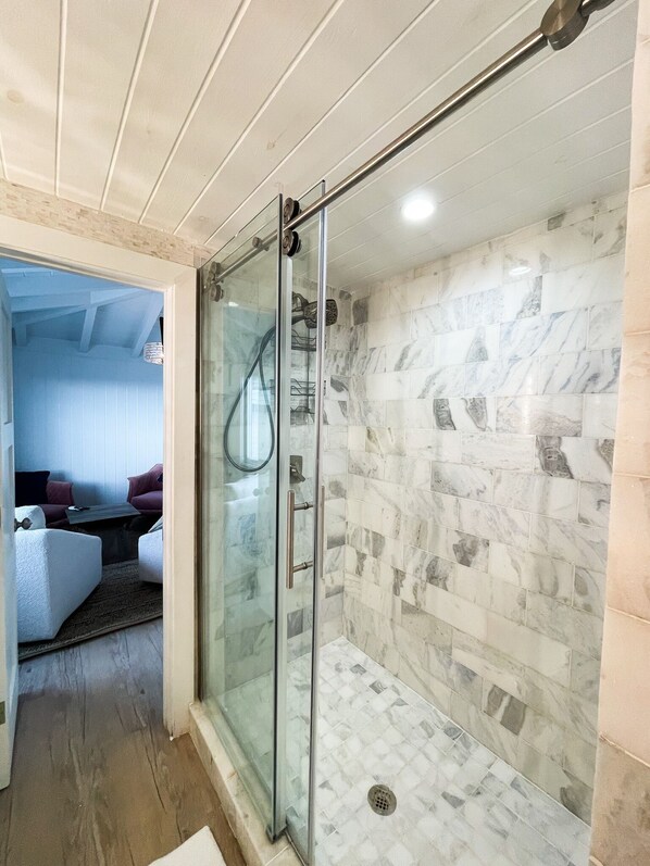 A modern bathroom with a glass-enclosed shower, marble tiles, and a visible seating area with a sofa and coffee table. - Bunk bed Suite (Elbow Cay)