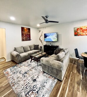 Ein Wohnzimmer mit einem Ecksofa, einem Couchtisch, einem Flachbildfernseher und einem Deckenventilator.