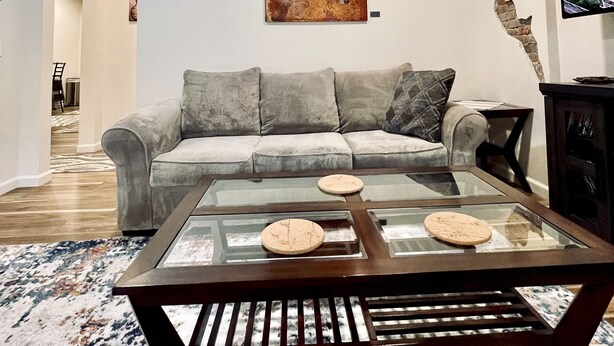 Een woonkamer met een grijze bank, een glazen salontafel en een schilderij aan de muur.