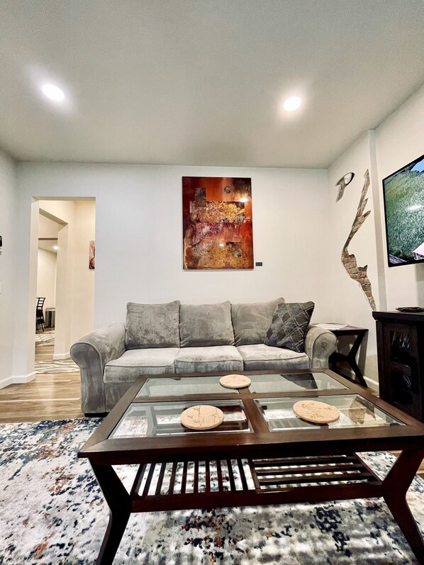 Ein Wohnzimmer mit einem grauen Sofa, einem Glastisch und einem Bild an der Wand.