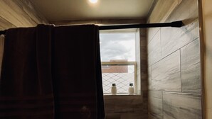Een badkamer met een douche, een handdoekhouder en een raam met uitzicht op gebouwen.