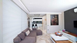 A modern living room with a grey sectional sofa, a white coffee table, and a flat-screen TV. - Villa Sole Sidyma – Luxury Villa with Heated Pool, Central Location, Bay Views (Antalya)