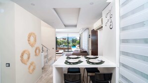 A modern dining area with a white table set for four, a staircase, and a view of a pool and greenery outside. - Villa Sole Sidyma – Luxury Villa with Heated Pool, Central Location, Bay Views (Antalya)