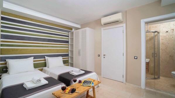 A hotel room with two beds, a wooden table with a magazine, a glass of wine, and a shower area.