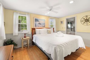 A bedroom with a bed, a ceiling fan, a window with curtains, a wall clock, and a compass decoration.