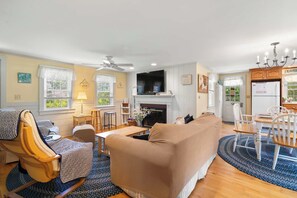 A living room with a fireplace, a dining area, and a kitchen with a refrigerator.