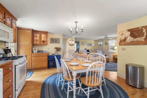 Una cocina amplia con armarios de madera, un comedor con mesa de madera y sillas blancas, y una araña.