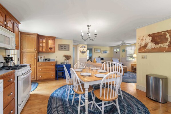 Una cocina amplia con armarios de madera, un comedor con mesa de madera y sillas blancas, y una araña.