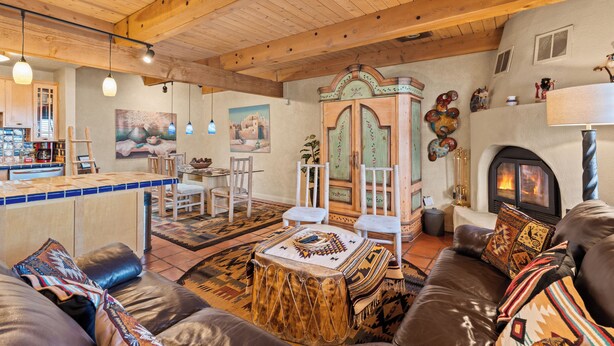A cozy living room with a fireplace, wooden ceiling beams, and a bar area.