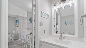A bathroom with a large mirror, white vanity, and a shower area. - 2BR Updated Condo | 2 Pools, Steps to Beach (Miramar Beach)