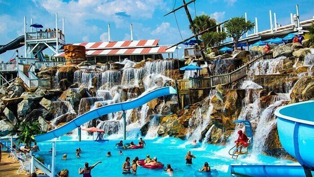 A water park with a large pool, multiple slides, and a waterfall. - 2BR Updated Condo | 2 Pools, Steps to Beach (Miramar Beach)
