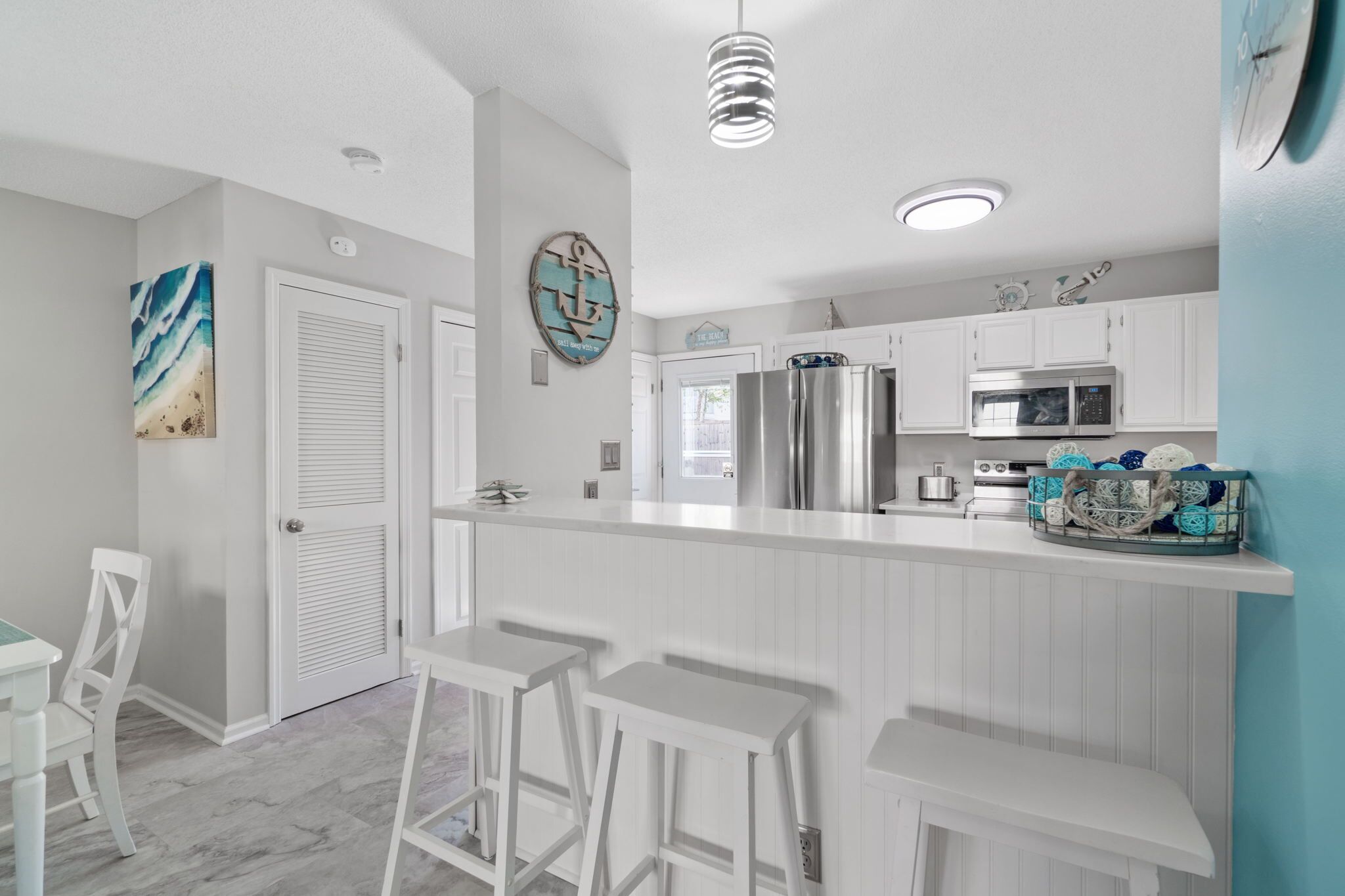 A modern kitchen with white cabinetry, stainless steel appliances, and a bar area with white stools.
