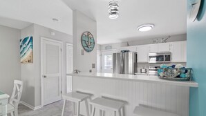 A modern kitchen with white cabinetry, stainless steel appliances, and a bar area with white stools. - 2BR Updated Condo | 2 Pools, Steps to Beach (Miramar Beach)