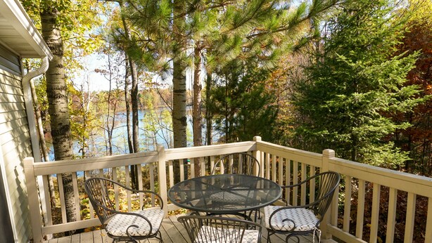 A wooden deck with a round table and four chairs, surrounded by trees and a lake view. - 2500 SF Remodeled Cottage on a Quiet Lake in the Woods (Rhinelander)
