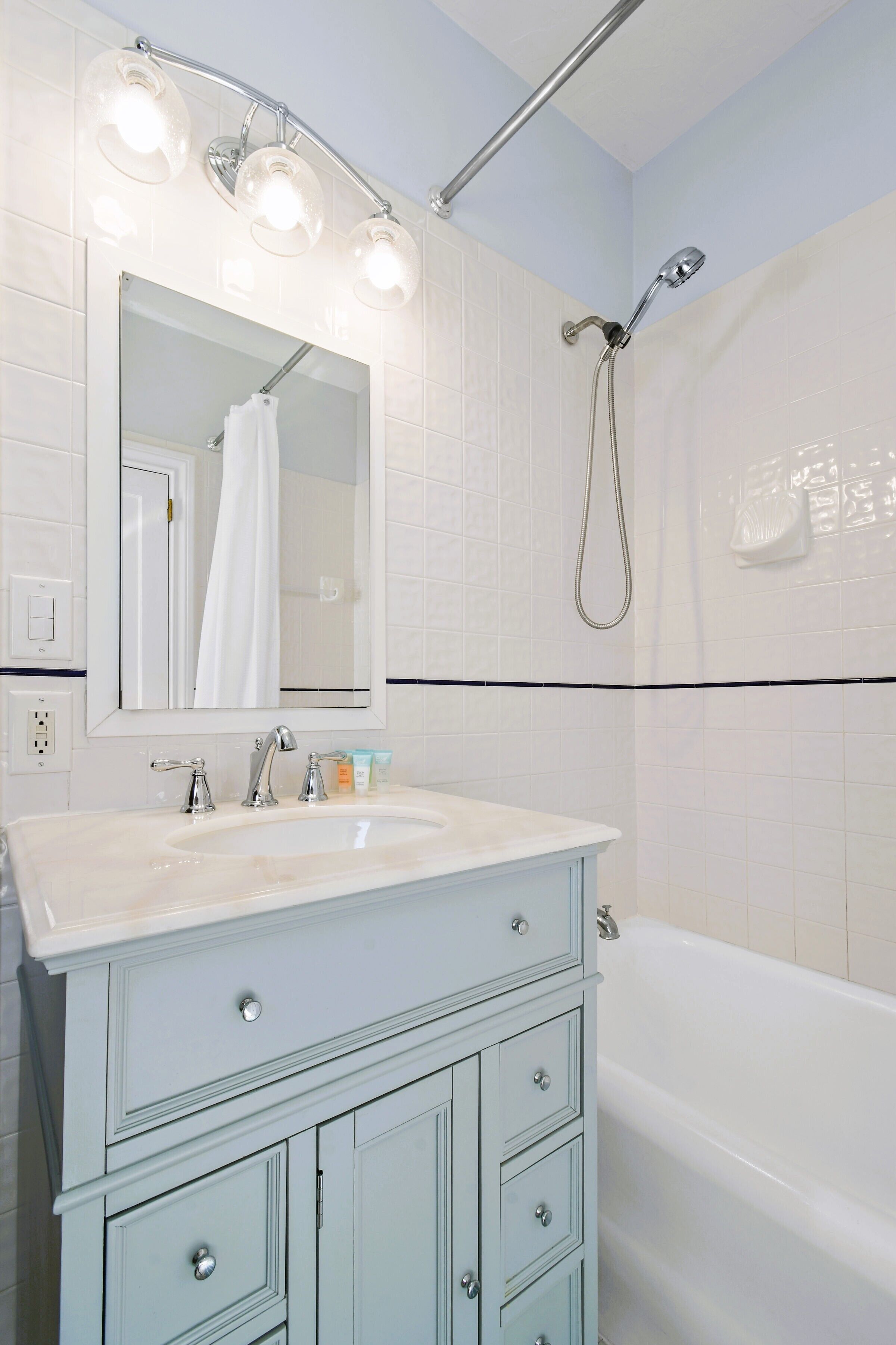 A bathroom with a white sink, a mirror with lights, a shower, and a bathtub.
