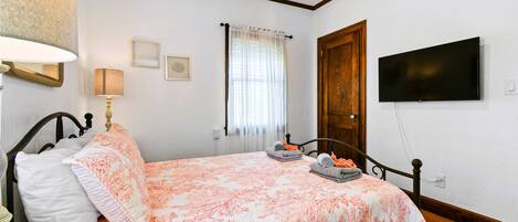 Un dormitorio con una cama, televisión, ventana con cortinas y una puerta de madera.