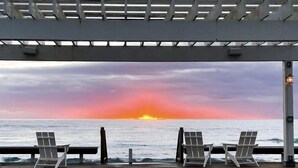 Een steiger met een metalen hekwerk en twee lege stoelen die uitkijken over de oceaan bij zonsondergang.