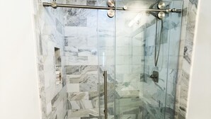 Een badkamer met een douchecabine van glas, marmeren tegels en een wit toilet.