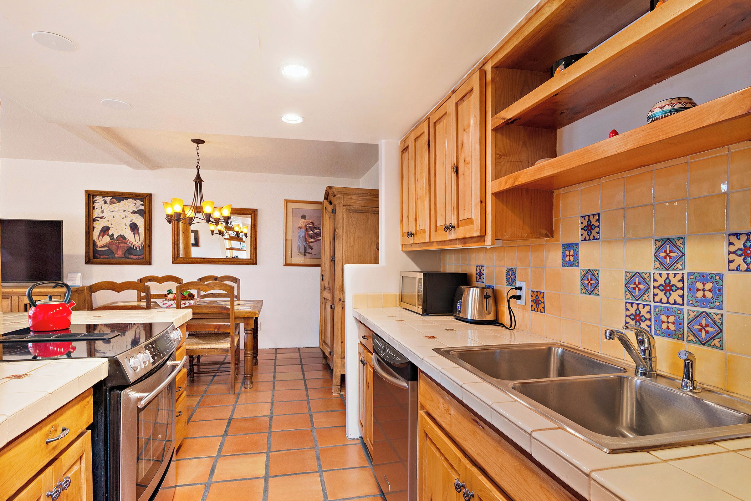 Una cocina con armarios de madera, microondas, fregadero y hervidor rojo.