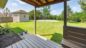A covered patio area with a basketball hoop, a wooden deck, and a well-maintained lawn.