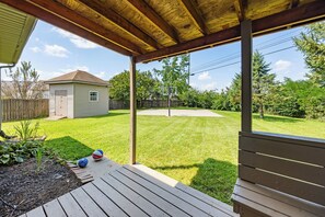 A covered patio area with a basketball hoop, a wooden deck, and a well-maintained lawn.