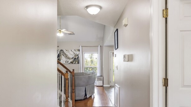 A hallway with wooden flooring, a ceiling fan, and a door on the right.