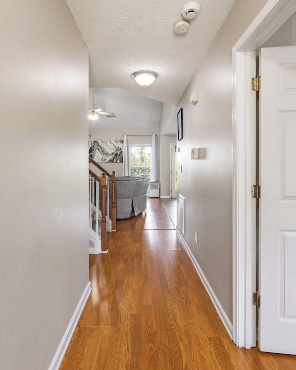 A hallway with wooden flooring, a ceiling fan, and a door on the right.