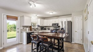 A kitchen with white cabinets, a central island with stools, stainless steel appliances, and a view to the outside.