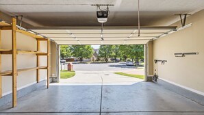 A garage with a concrete floor, wooden shelving, a ceiling-mounted projector, and a view of a residential street with houses and trees.