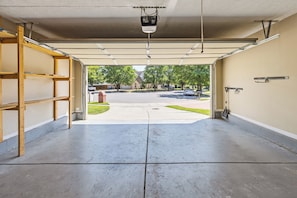 A garage with a concrete floor, wooden shelving, a ceiling-mounted projector, and a view of a residential street with houses and trees.