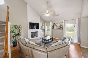 Un salón amplio con chimenea, un sofá grande, un televisor de pantalla plana y un ventilador de techo.