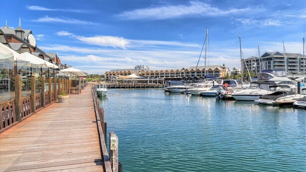 A marina with docked boats, a wooden pier, and a row of buildings with a distinctive architectural style.