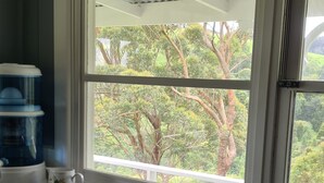 A kitchen with a double sink, a window with a view of trees, and a coffee maker on the counter. - Foster - Nature Retreat -  Nippards Nature Cottage (Woorarra West)