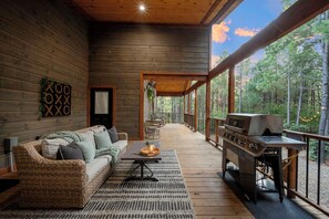 Ein Holzblockhaus-Innenraum mit einer Couch, einem Grill und Blick auf den Wald.