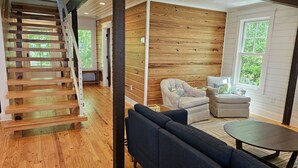 Een modern interieur met een houten wenteltrap, een gezellige zithoek met een ronde tafel, en grote ramen met uitzicht op groen.