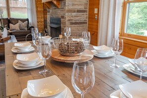 A wooden dining table set with white plates, bowls, and wine glasses, centered around a wire basket.